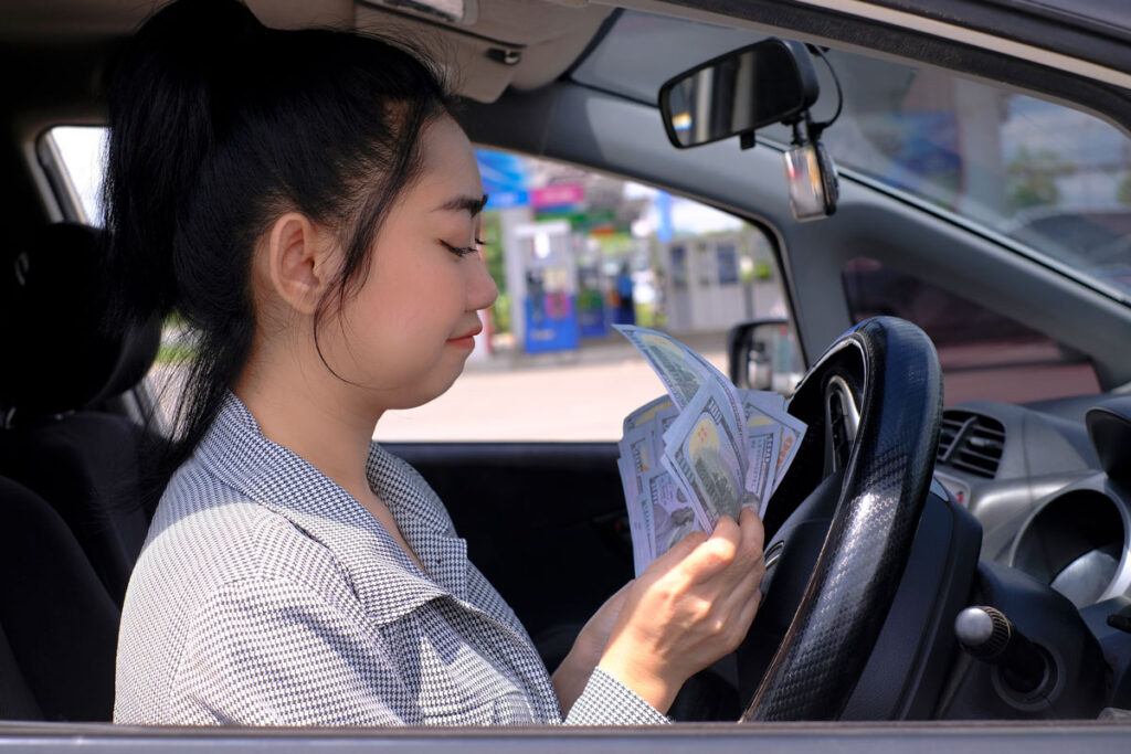 An asian woman counting cash inside a used car