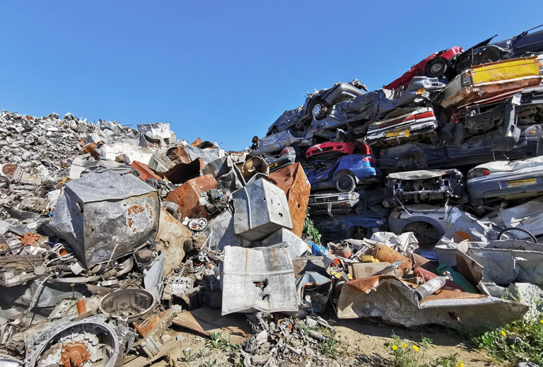 A pile of scrap metal and old crushed cars in different colors against a blue sky